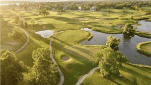 Aerial view of Geneva Golf Club with fairways, sand bunkers, and water features at sunset.