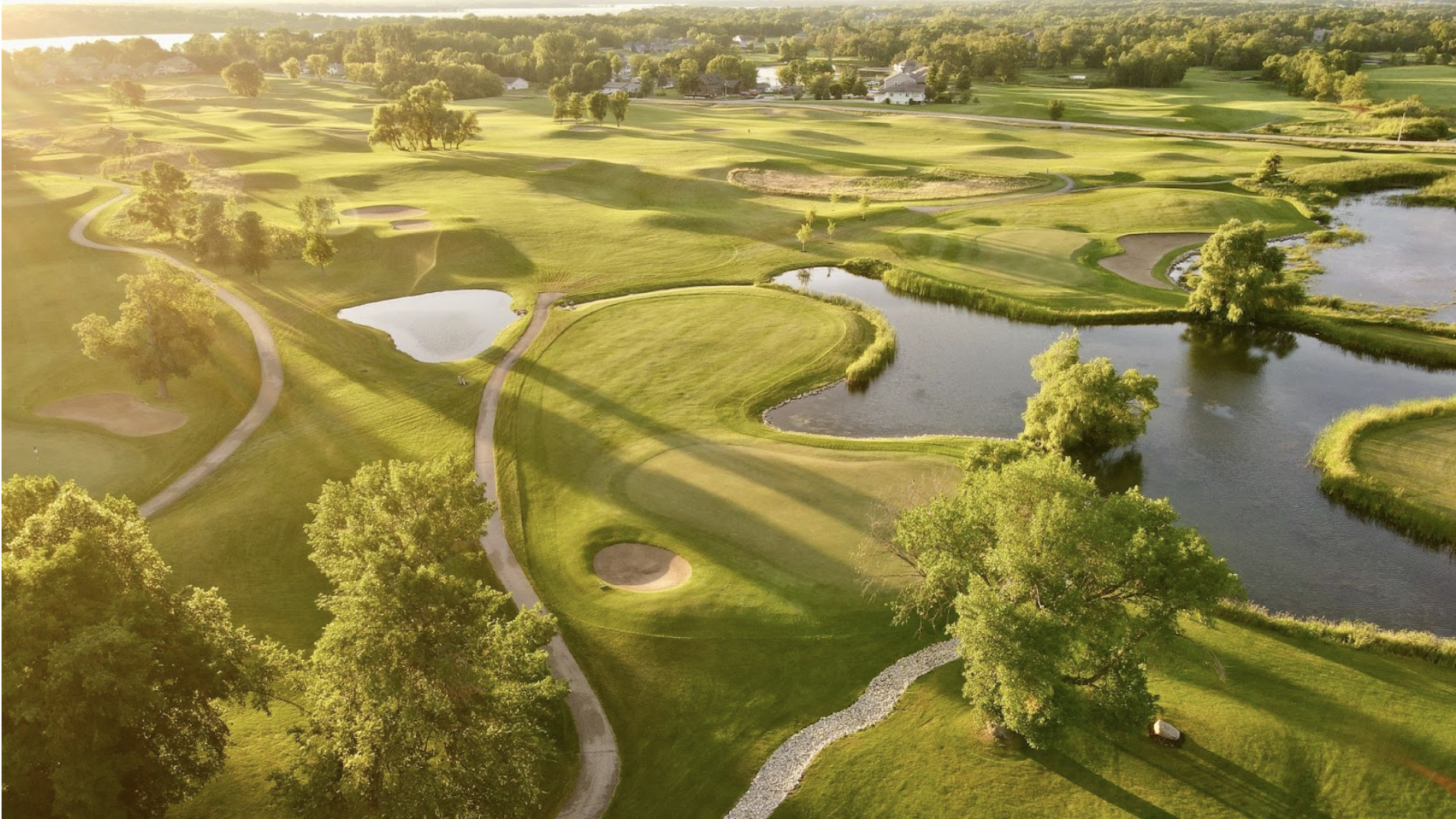 Aerial view of Geneva Golf Club with fairways, sand bunkers, and water features at sunset.
